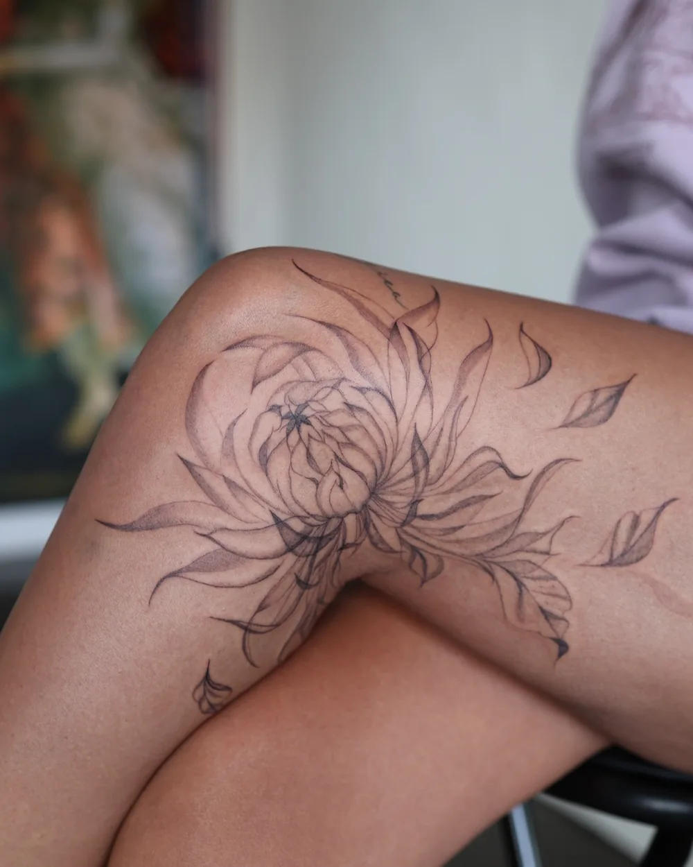 A fine line chrysanthemum tattooed across a thigh.