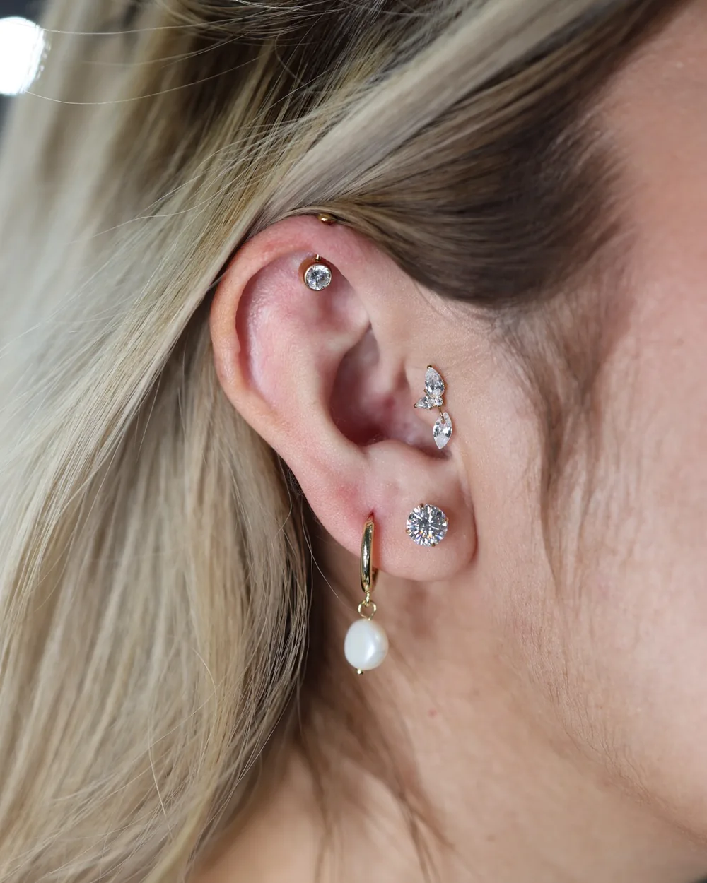 A curated ear with a stone cluster and a pearl drop, in gold.