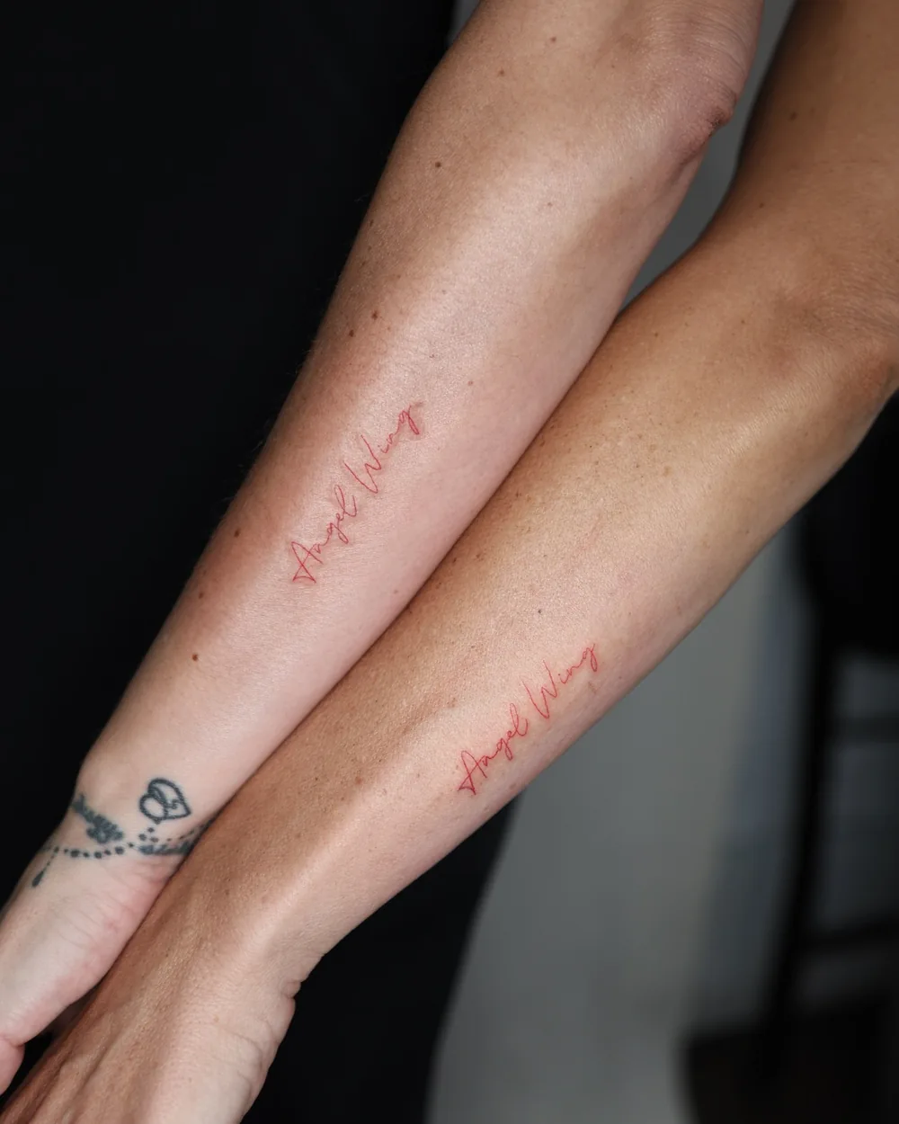 Matching fine line script tattooed on two forearms.