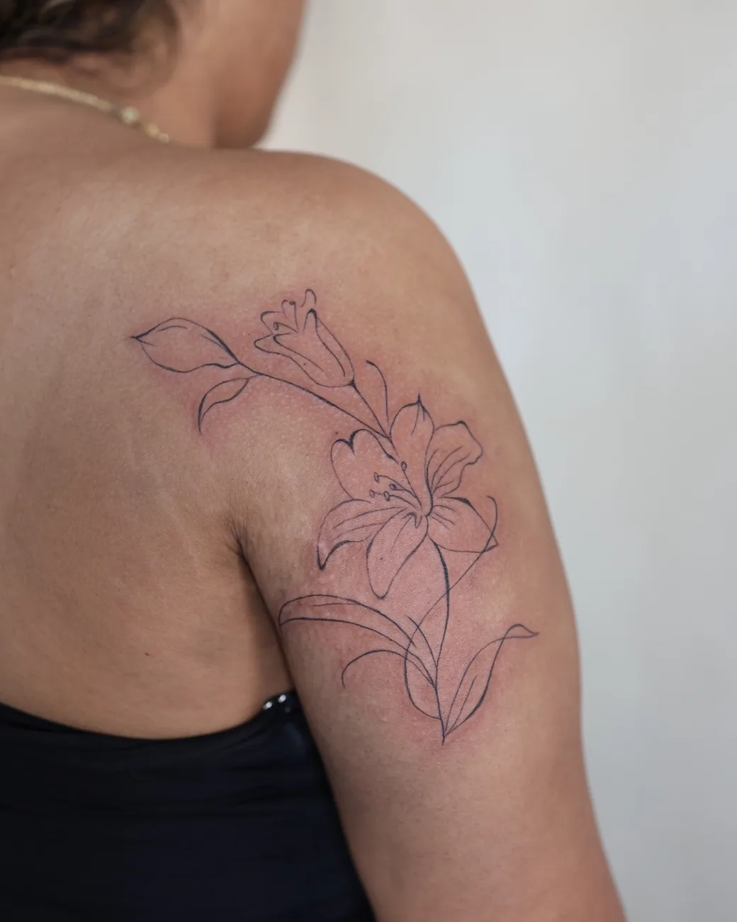 A fine line lily tattooed across a shoulder.